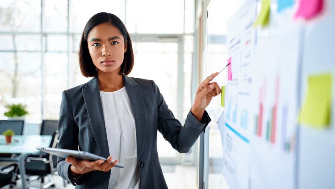 Femme souriante en pull jaune pointant vers la droite sur fond bleu, pour illustrer une formation en gestion d’entreprise proposée par CréActifs.