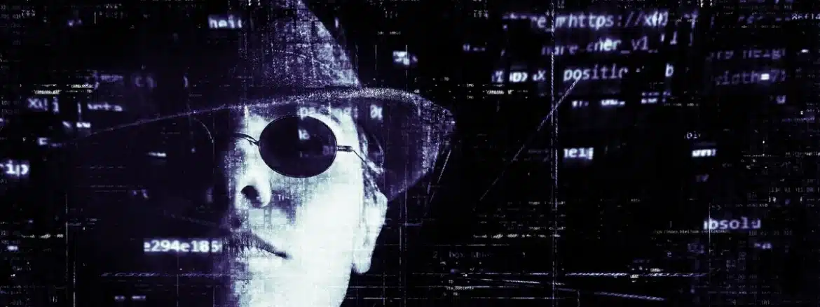 Personne anonyme devant un ordinateur portable dans une pièce sombre, symbolisant l'activité criminelle en ligne