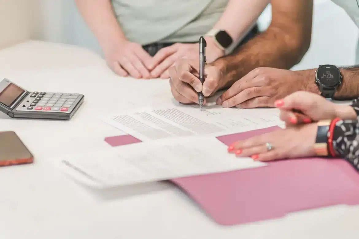 Mains triant des documents d'assurance sur une table ensoleillée près d'une fenêtre